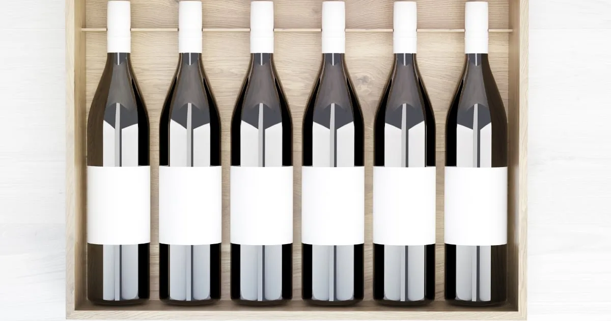A wooden crate of six wine bottles, each carrying a blank white label ready to be printed